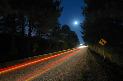 Cars pass on a country road at night with the moon above