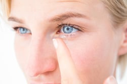 Pretty blonde applying contact lens on white background